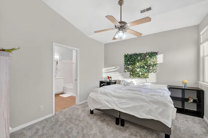 Bedroom featuring vaulted ceiling, light colored carpet, ensuite bath, and ceiling fan