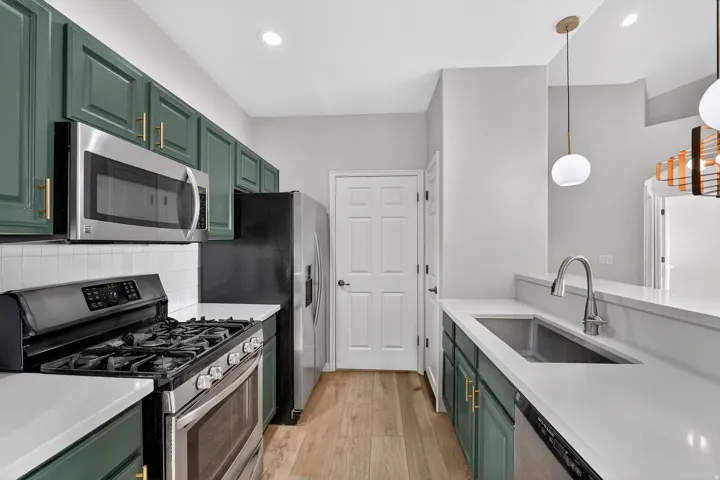 Kitchen with green cabinets, stainless steel appliances, light wood-style flooring, hanging light fixtures, and light stone countertops
