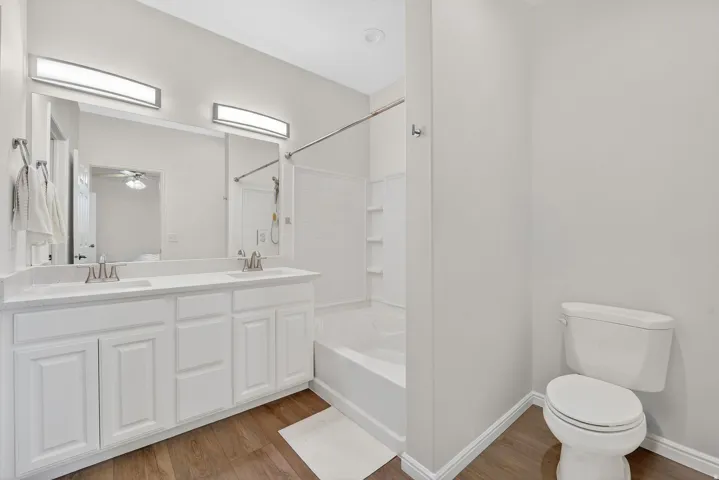 Bathroom with double vanity, light wood-style flooring, ceiling fan, and shower / bath combination