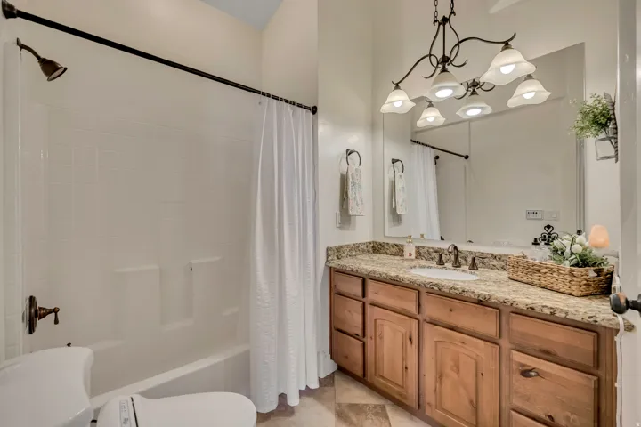 Bathroom with vanity, shower / tub combo with curtain, and suspended lighting
