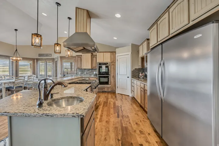 Kitchen with stainless steel appliances, pendant lighting, light stone countertops, light wood-style flooring, and backsplash