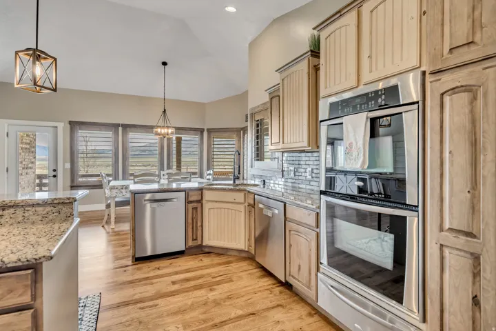 Kitchen with stainless steel appliances, hanging lights, a warming drawer, light wood finish cabinetry, and vaulted ceiling