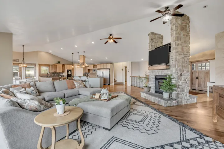 Living room featuring vaulted ceiling, light wood-type flooring, ceiling fan, suspended lighting, and a stone fireplace