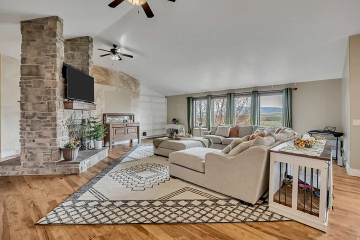 Living room featuring a fireplace, light wood-style flooring, lofted ceiling, and a ceiling fan