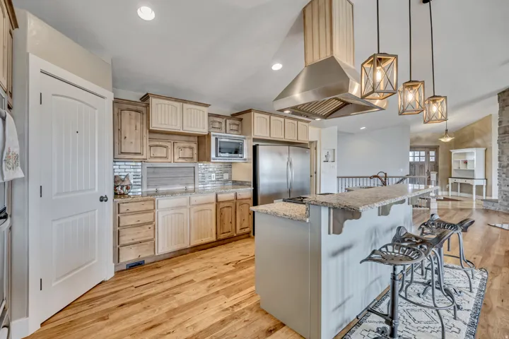 Kitchen with light wood-style flooring, a kitchen bar, light stone countertops, decorative light fixtures, and island range hood