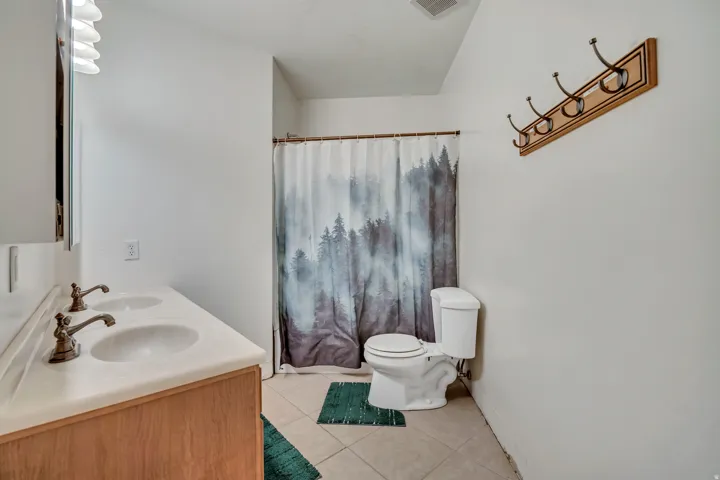 Bathroom featuring double vanity, light tile patterned floors, and a shower with shower curtain