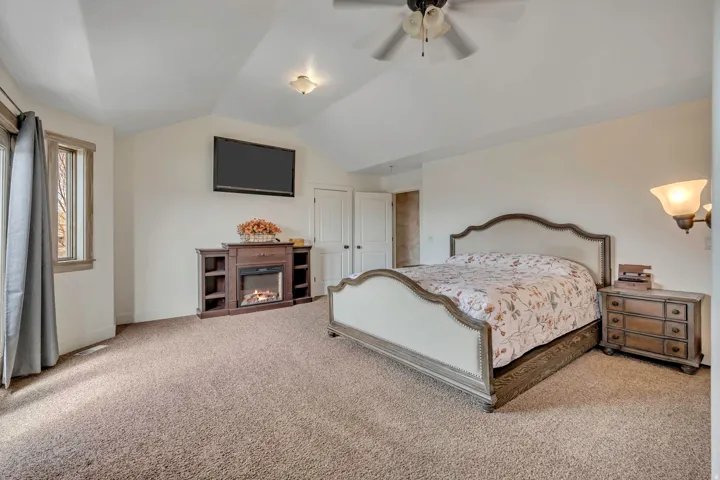 Bedroom featuring carpet flooring, ceiling fan, and a glass covered fireplace