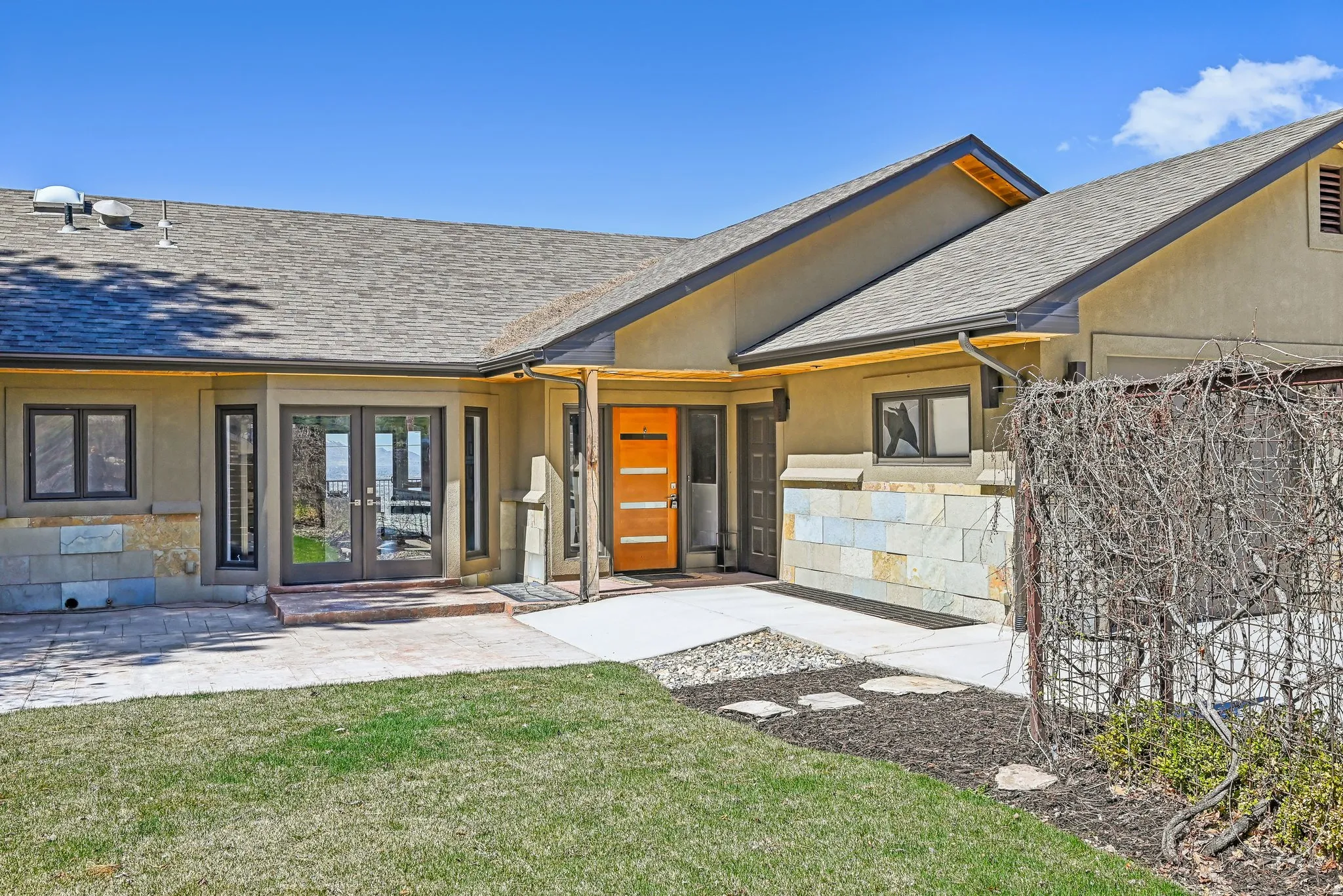 Property entrance featuring stone siding, french doors, stucco siding, roof with shingles, and a yard