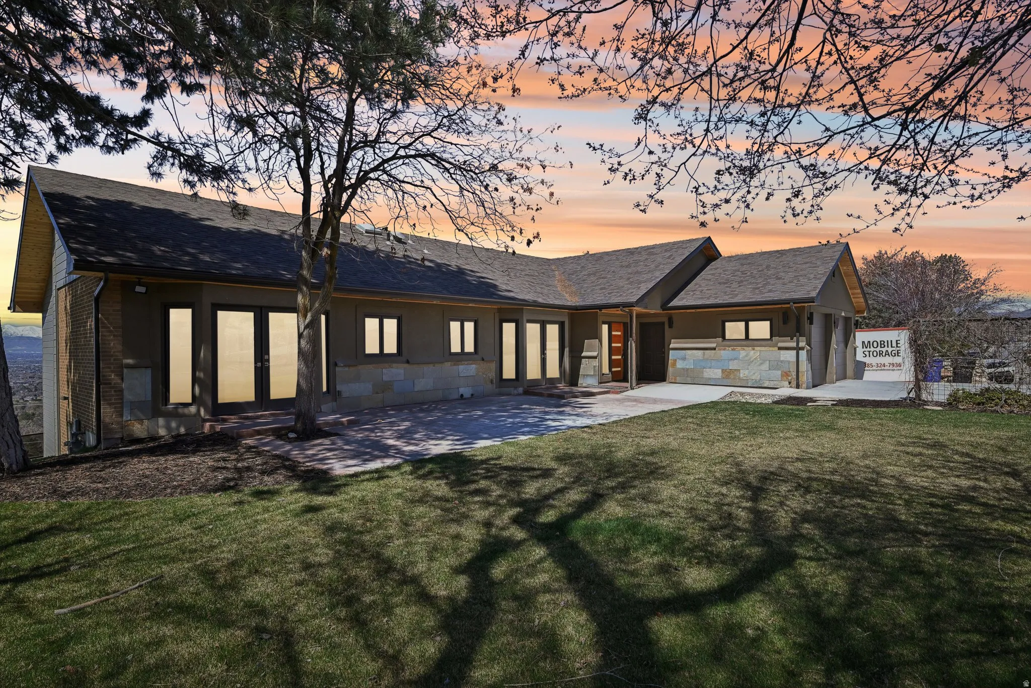 Back of property at dusk featuring french doors, a lawn, stone siding, and a shingled roof