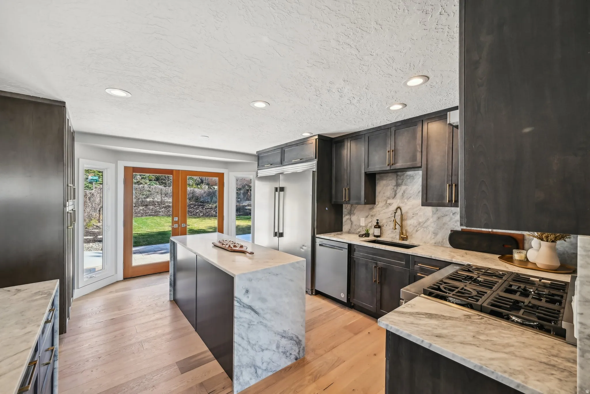 Kitchen featuring light stone counters, light wood-style floors, stainless steel appliances, a textured ceiling, and french doors