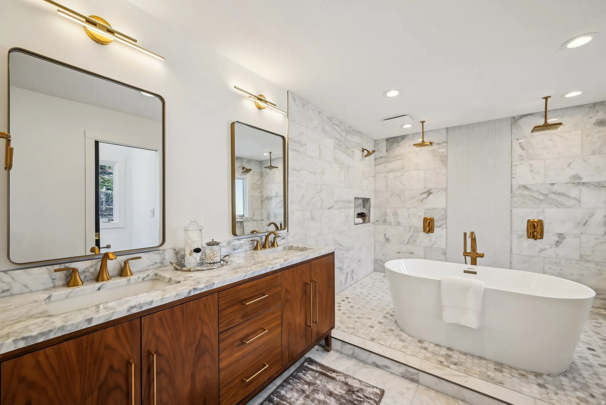 Primary bathroom with double vanity, Carrera marble, standing tub, natural light, toilet room with fan.