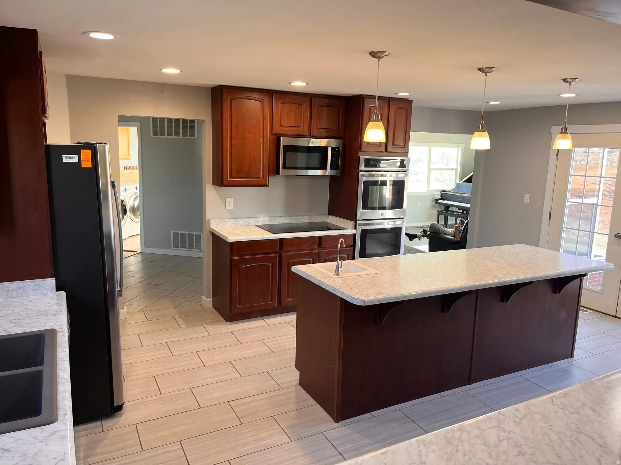 Kitchen featuring stainless steel appliances, hanging light fixtures, a kitchen breakfast bar, wood finish floors, and washing machine and clothes dryer