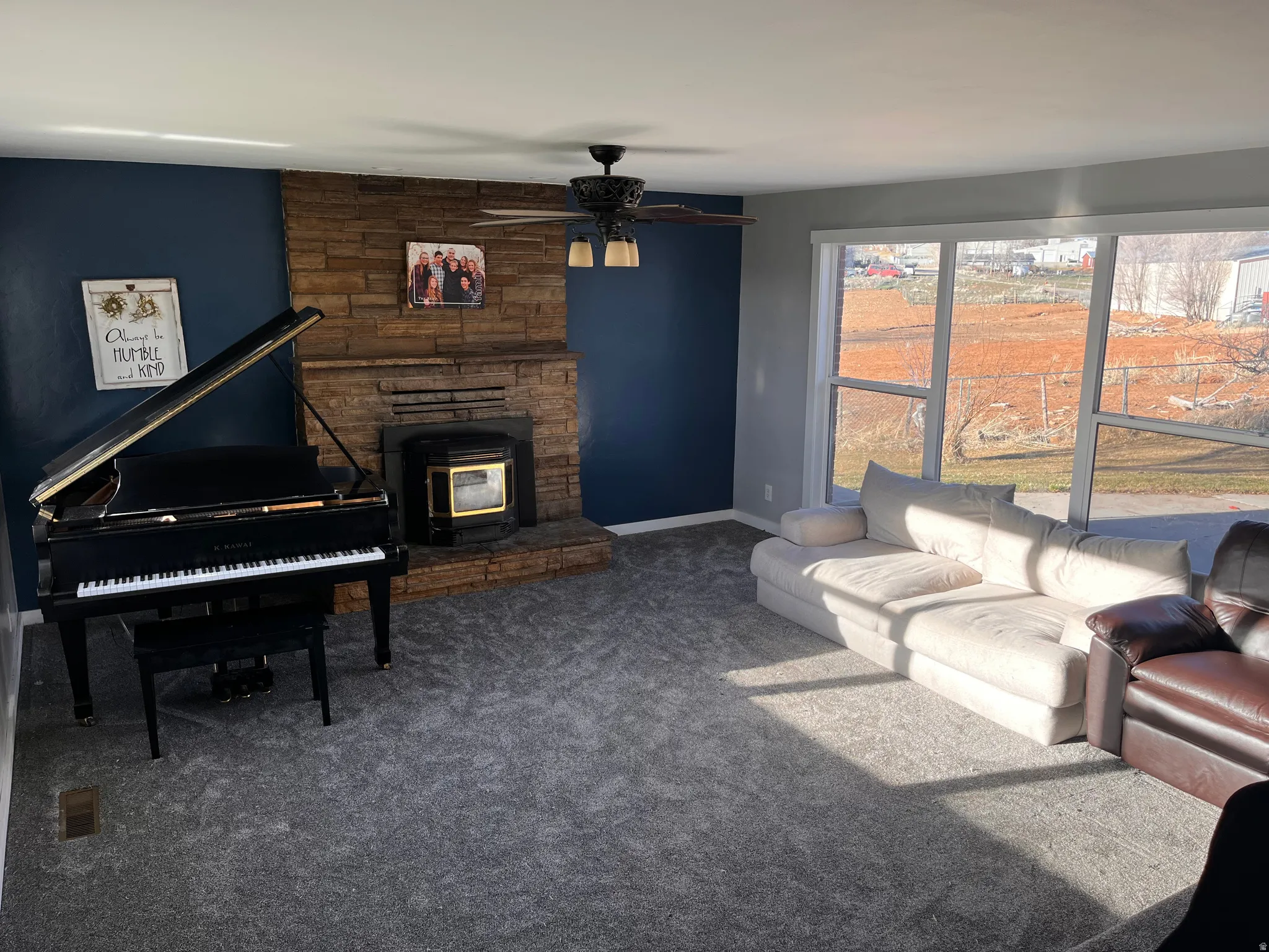 Carpeted living room featuring a wood stove and a ceiling fan
