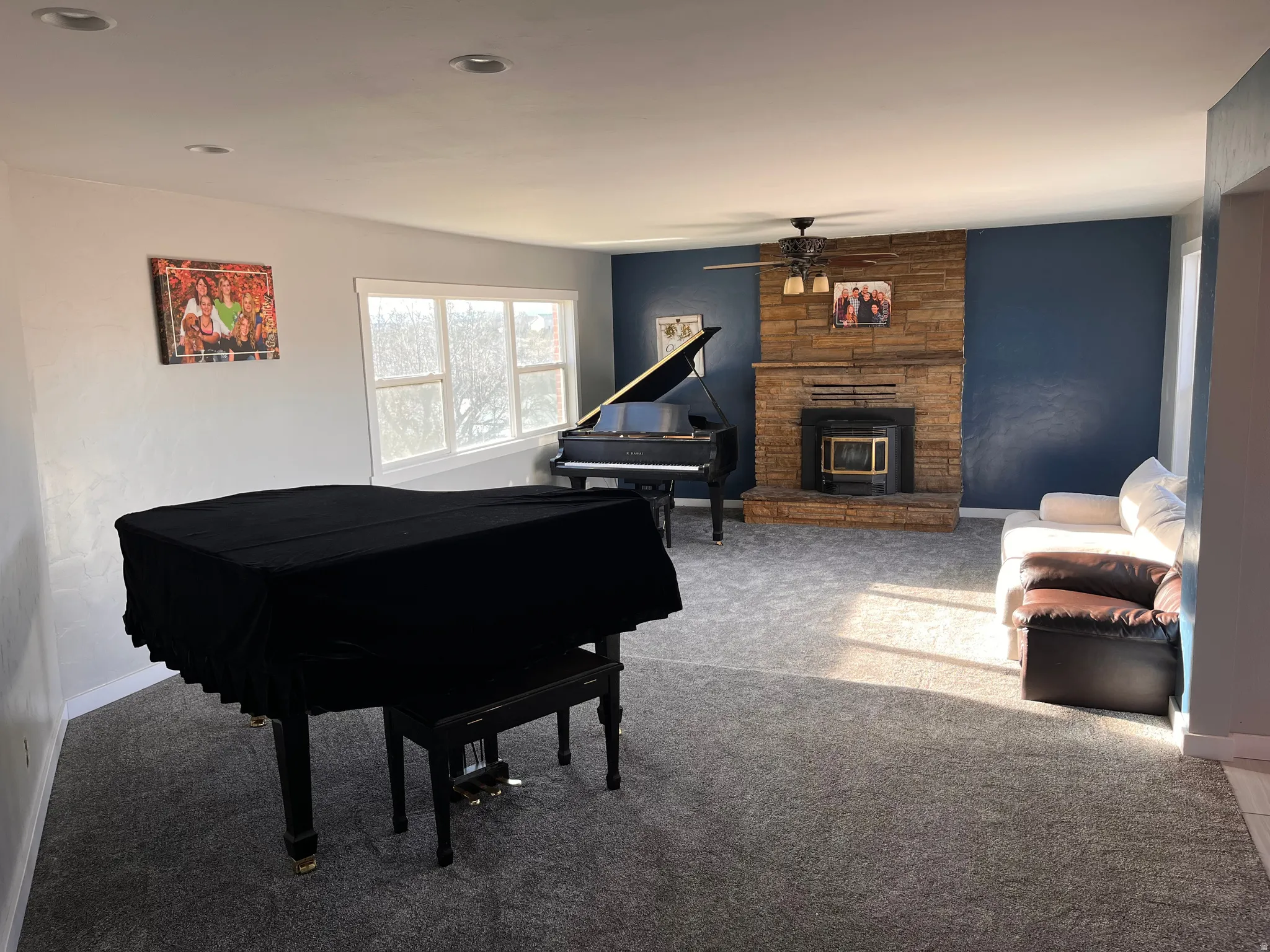 Living area with carpet floors, ceiling fan, and a stone fireplace