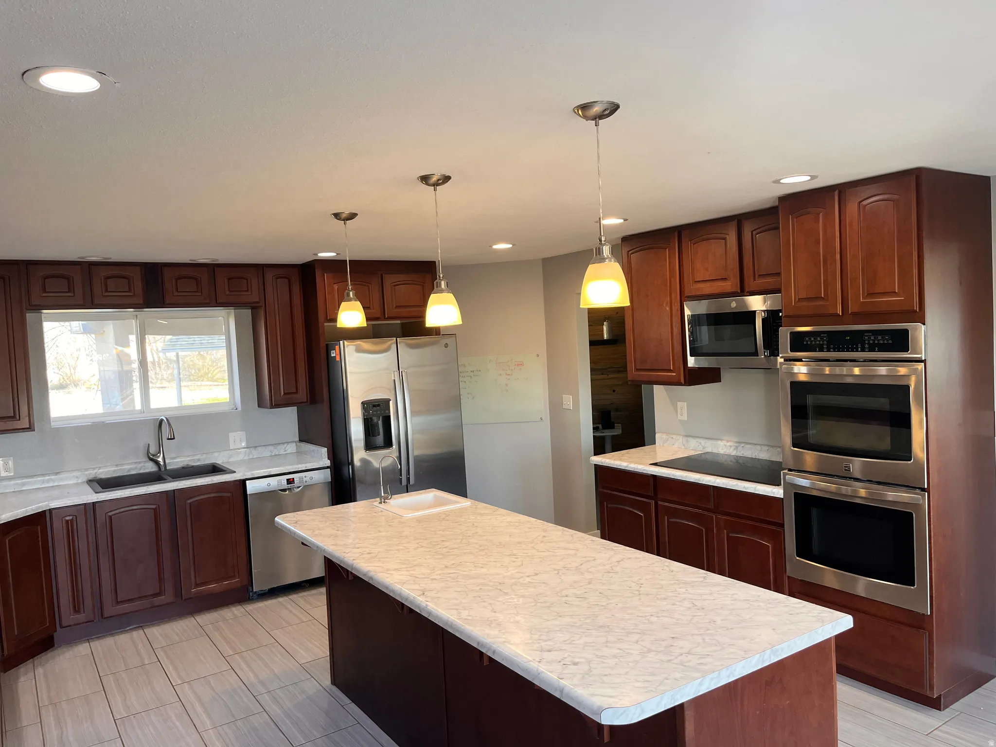 Kitchen featuring stainless steel appliances, a kitchen island, light countertops, pendant lighting, and dark wood finish cabinets