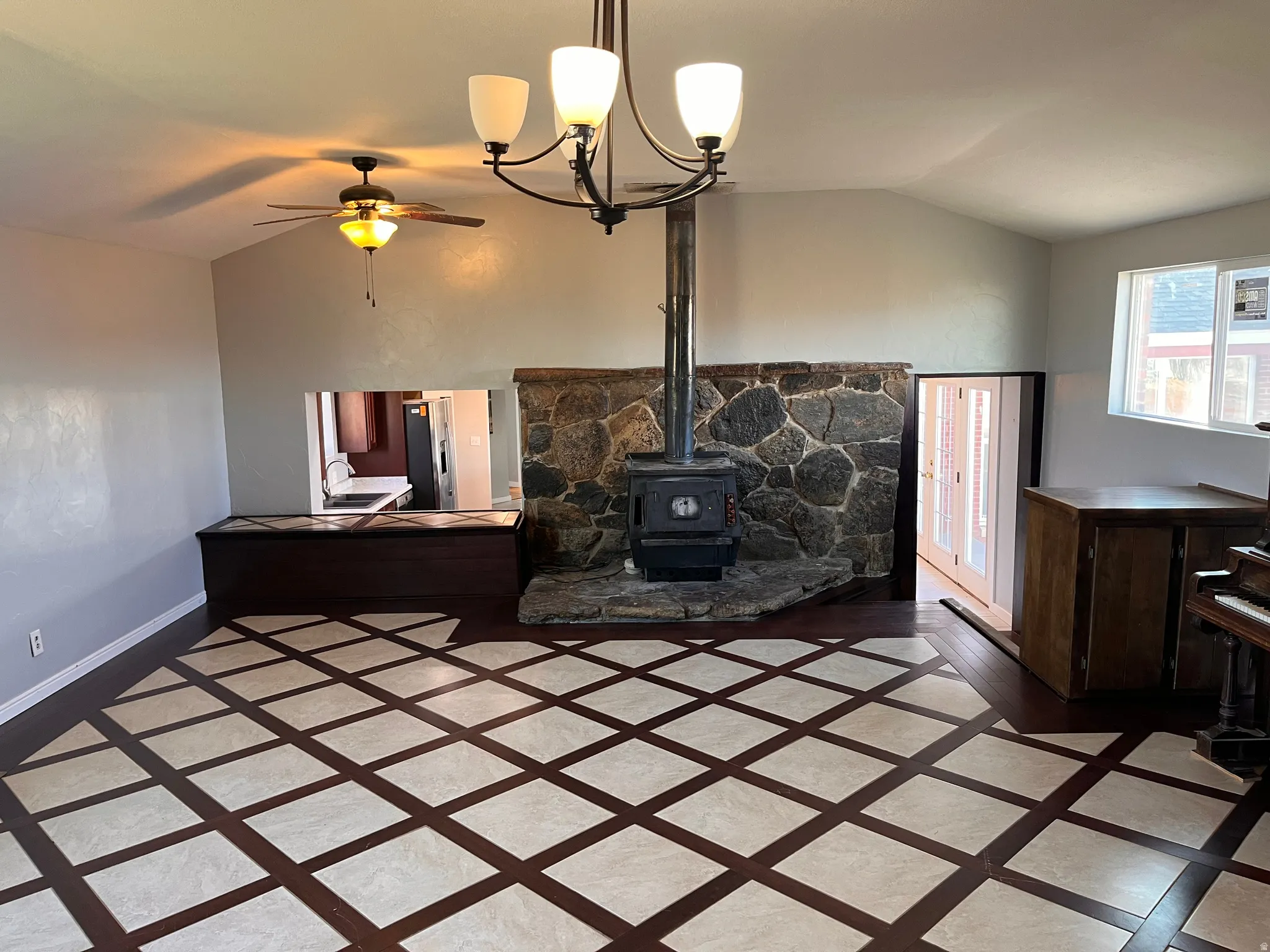 Living room featuring inlaid floor details, vaulted ceiling, ceiling fan, a wood stove, and a chandelier