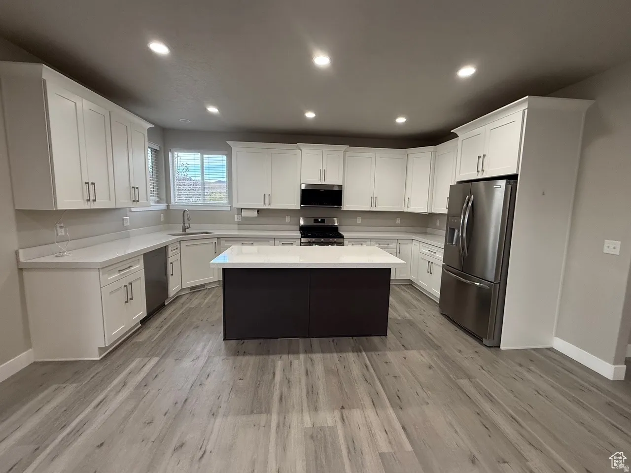 Two tone kitchen with stainless steel appliances, a center island, recessed lighting, light stone counters, and light wood finished floors