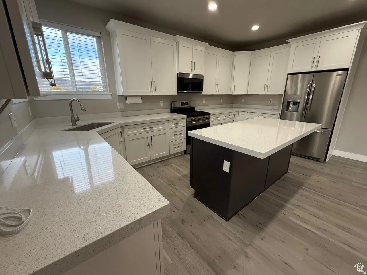 Two tone kitchen with stainless steel appliances, light stone counters, light wood finished floors, a center island, and recessed lighting