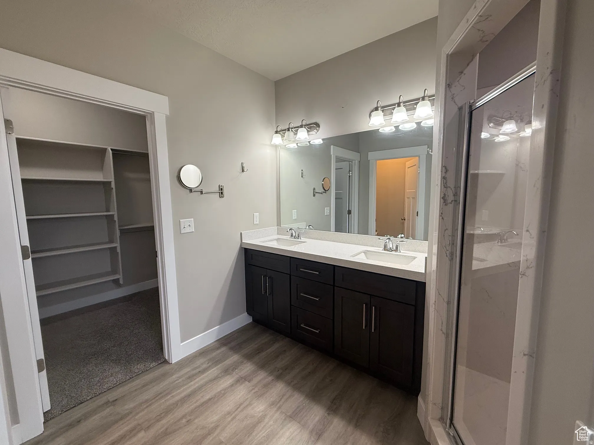 Full bathroom with a spacious closet, double vanity, a marble finish shower, and light wood-type flooring