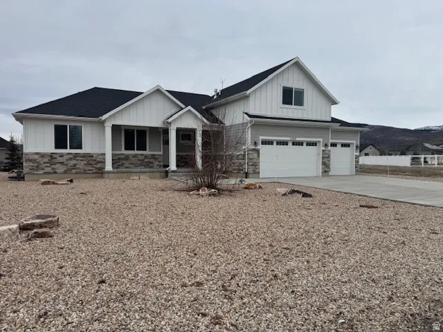 View of front of property featuring board and batten siding, an attached garage, a porch, stone siding, and concrete driveway