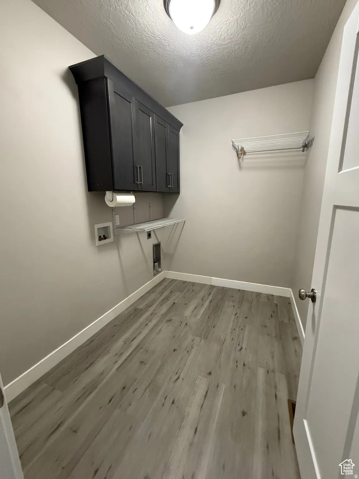 Laundry room with light wood-style floors, a textured ceiling, hookup for a washing machine, and cabinet space