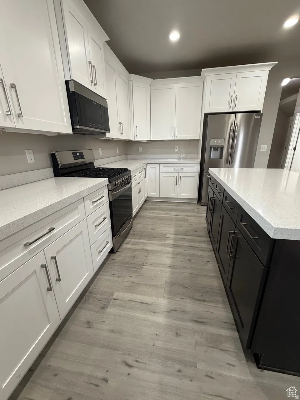 Kitchen featuring two tone color scheme, stainless steel appliances, light stone counters, recessed lighting, and light wood finished floors