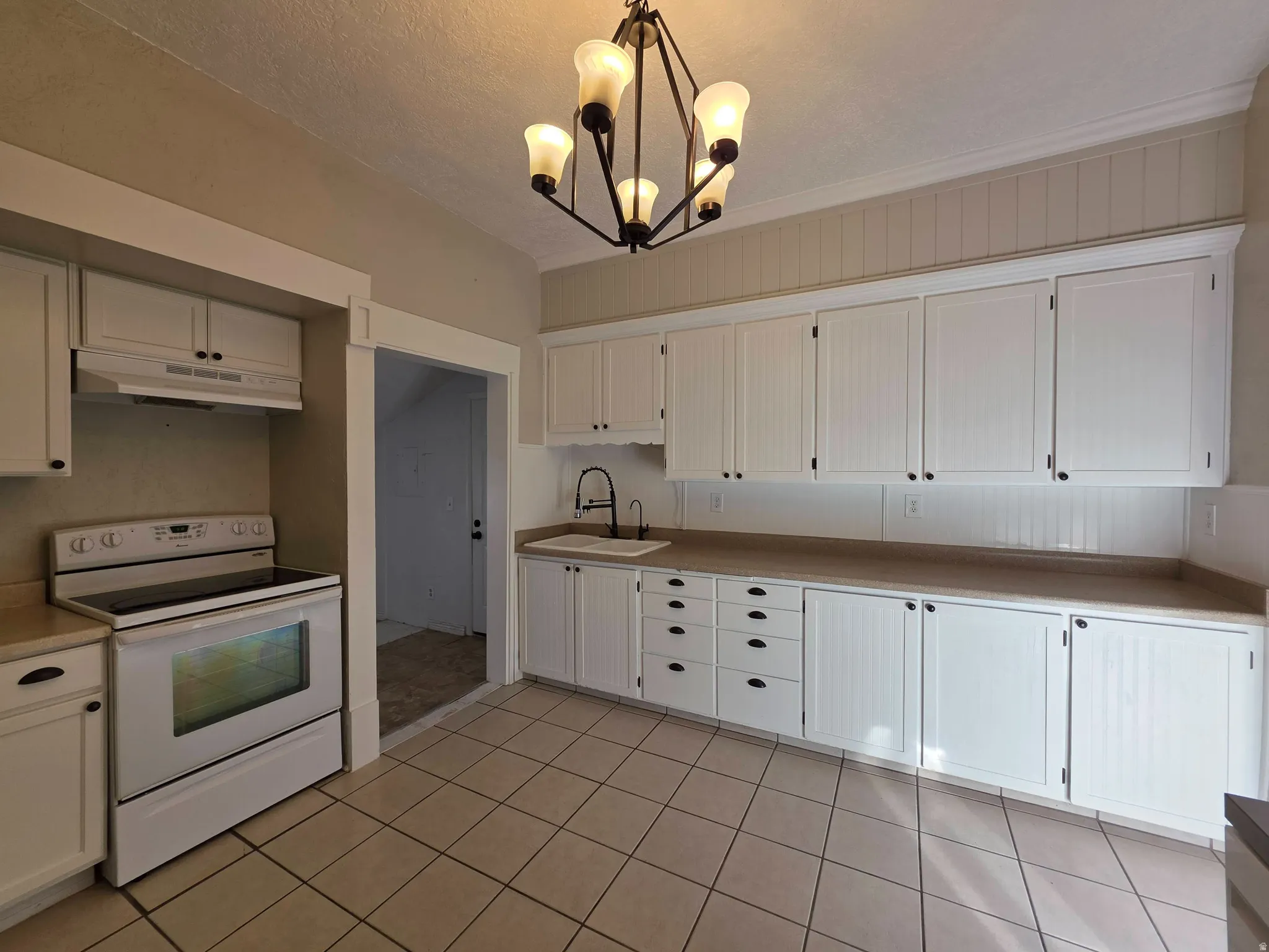 Kitchen with white range with electric stovetop, white cabinets, a chandelier, light countertops, and a textured ceiling