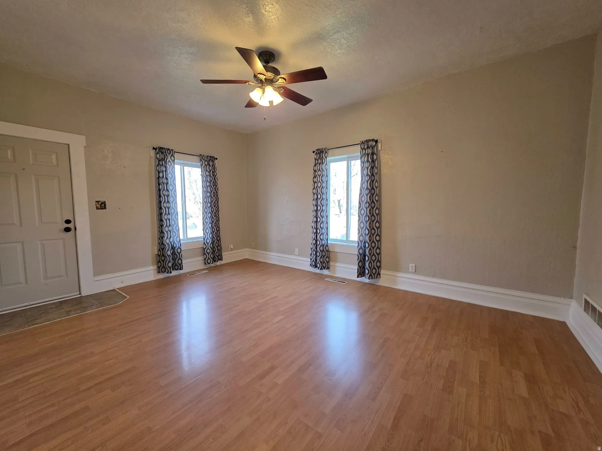 Spare room featuring light wood-style flooring, plenty of natural light, a ceiling fan, and a textured ceiling