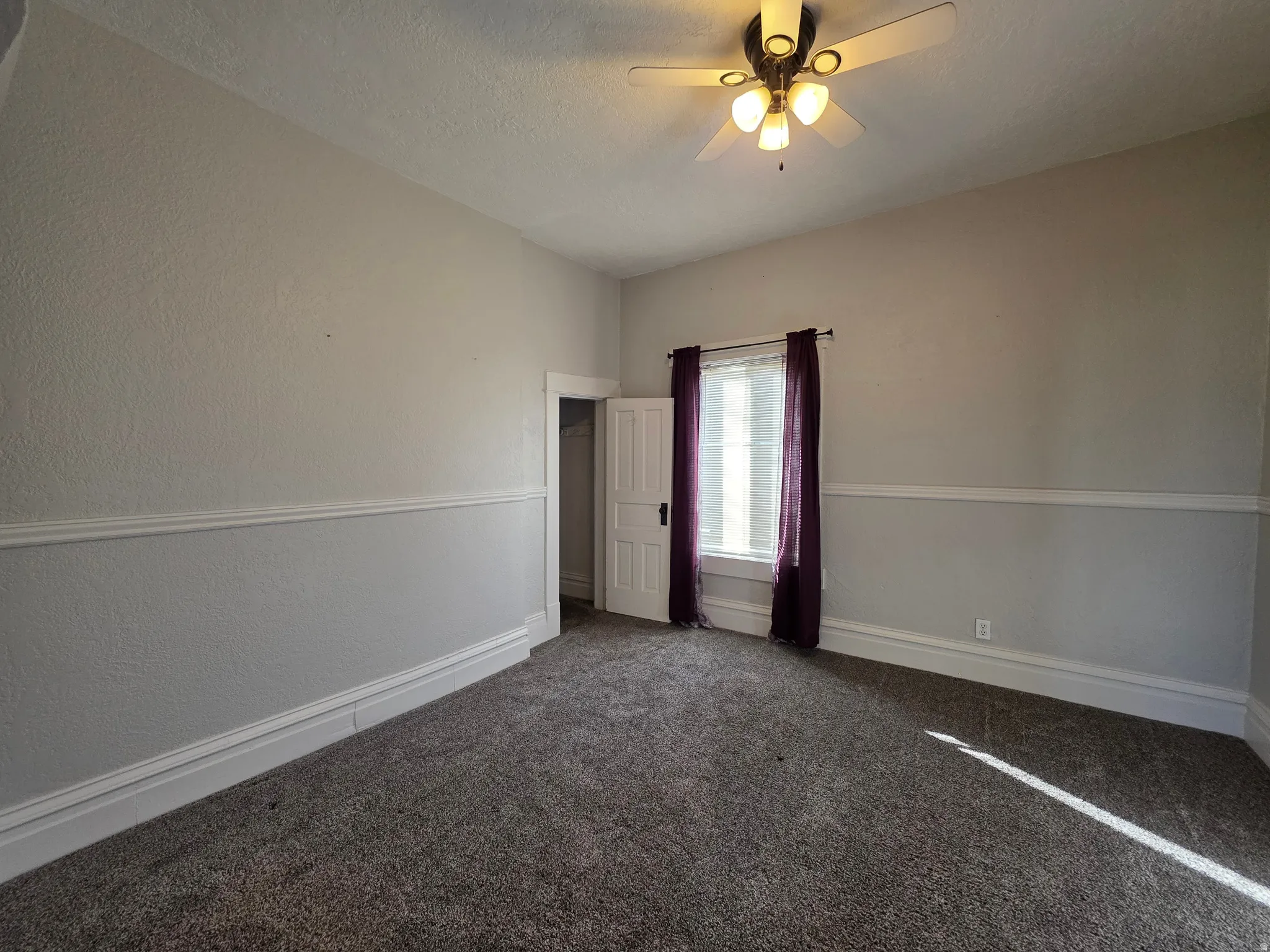 Carpeted empty room featuring a ceiling fan, a textured ceiling, and a textured wall