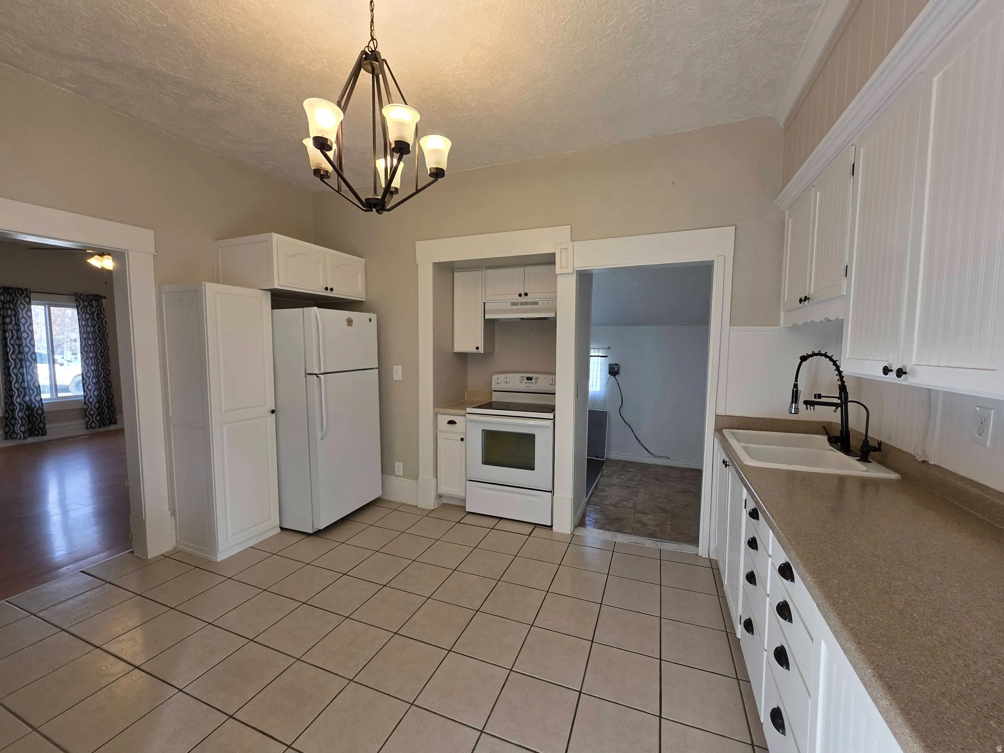 Kitchen featuring white appliances, white cabinetry, a textured ceiling, a chandelier, and light tile patterned flooring