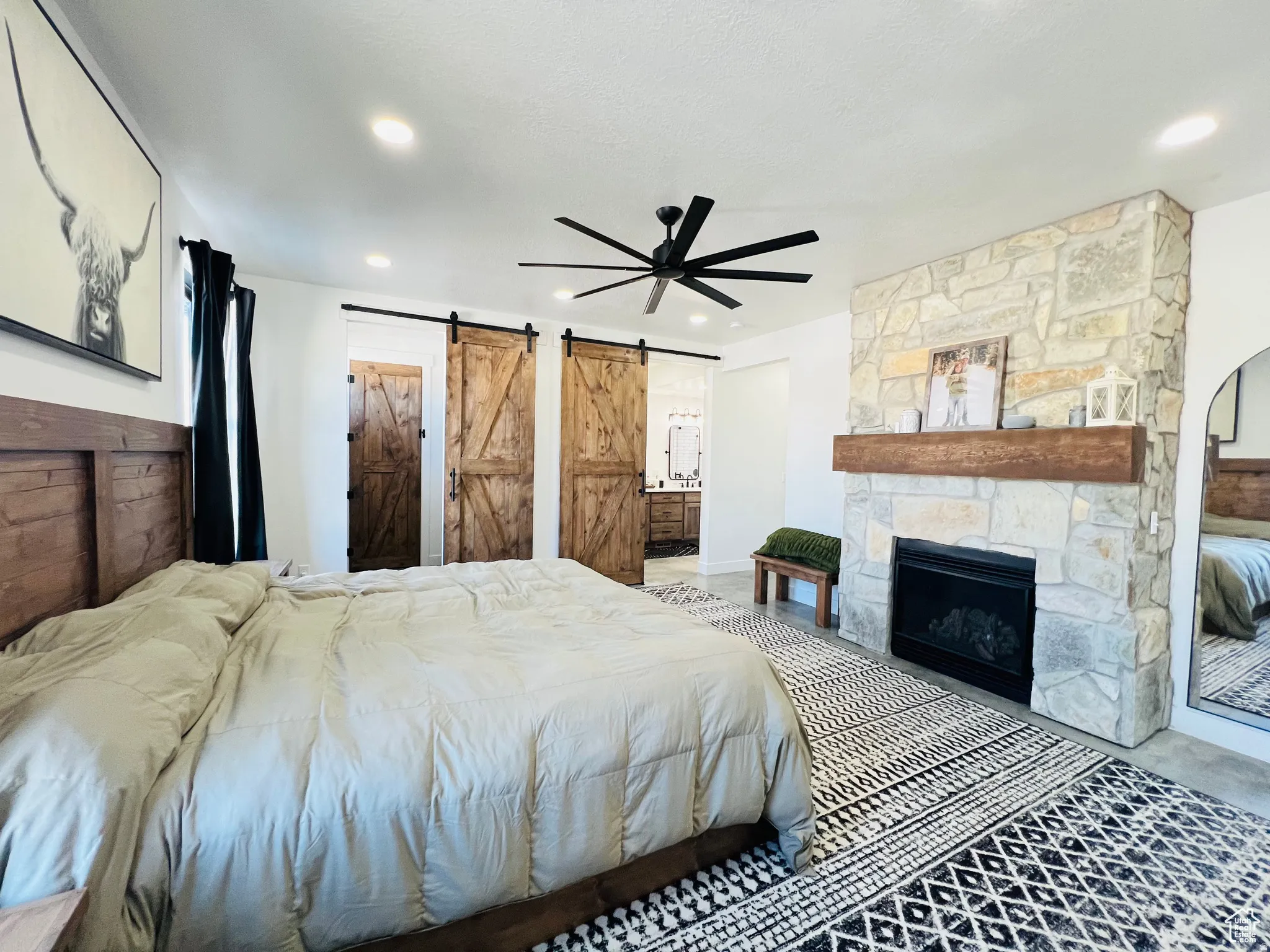 Bedroom with a barn door, a ceiling fan, a fireplace, and ensuite bath