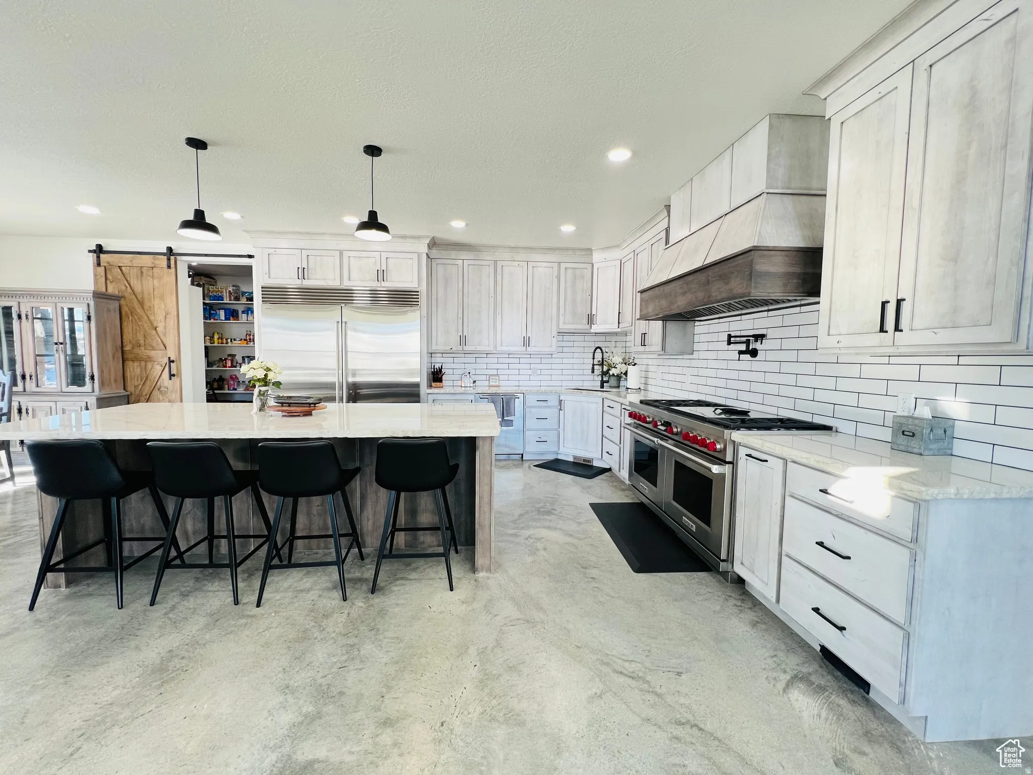 Kitchen featuring a barn door, high end appliances, light stone counters, decorative light fixtures, and a breakfast bar
