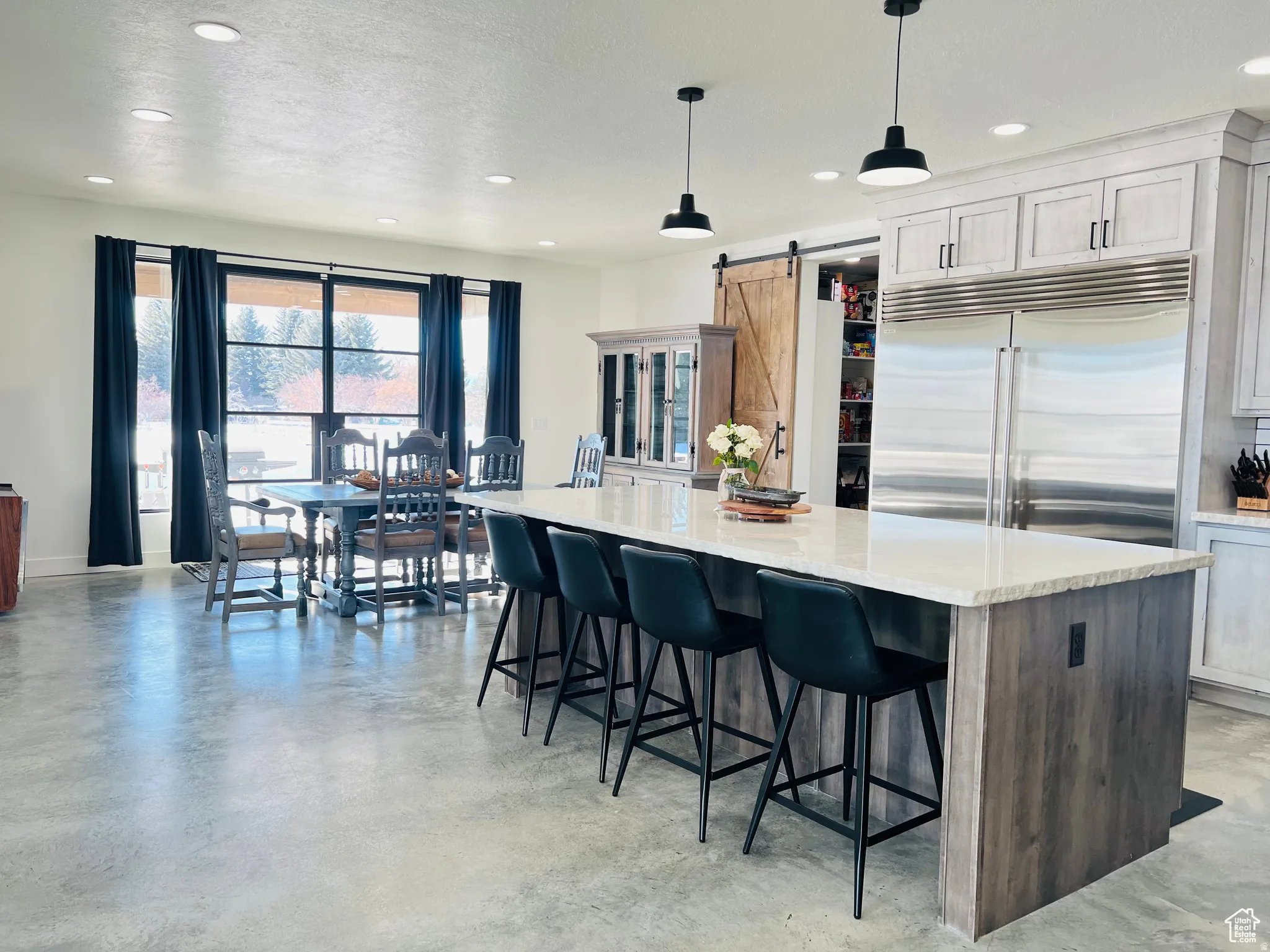 Two tone kitchen featuring finished concrete flooring, stainless steel built in fridge, a barn door, a kitchen island, and light stone counters