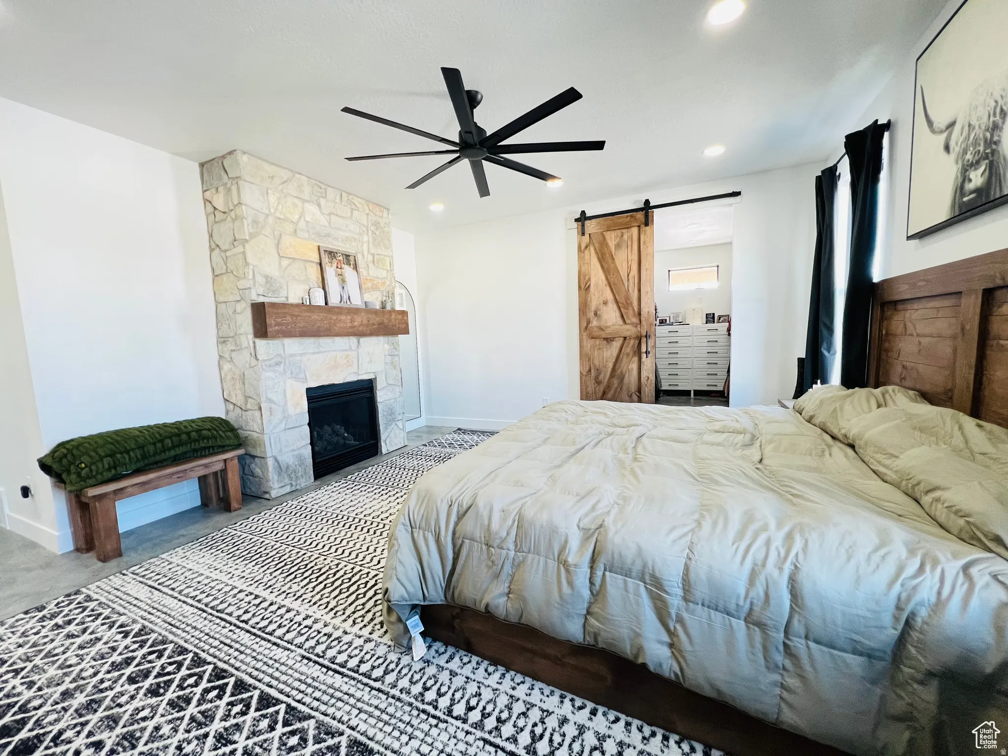 Bedroom with a barn door, a ceiling fan, and a stone fireplace