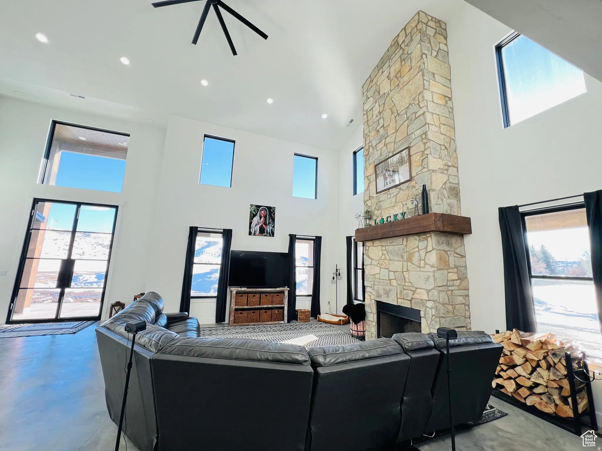 Living room featuring a high ceiling, finished concrete floors, ceiling fan, and a stone fireplace