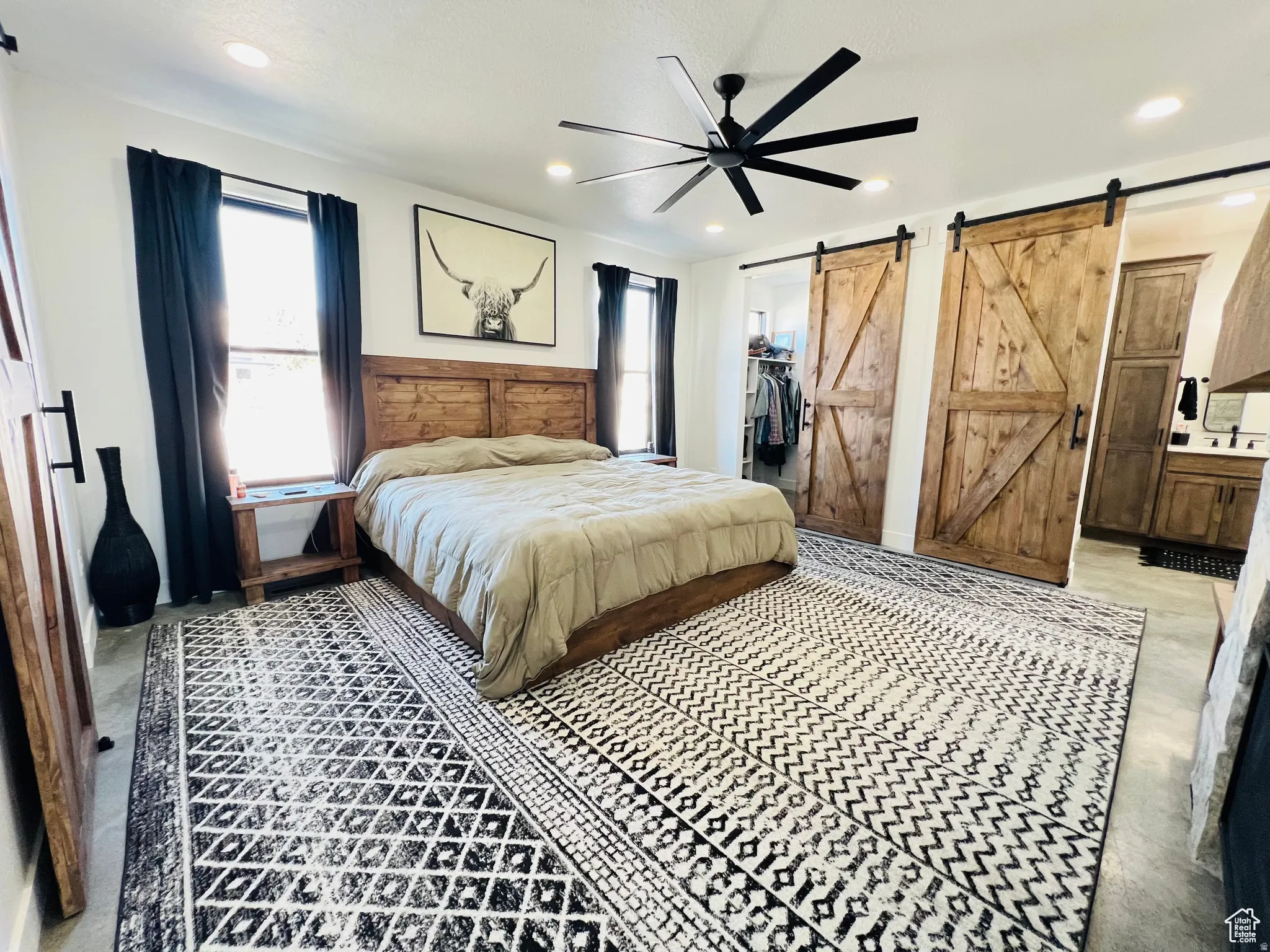 Bedroom featuring a barn door, a walk in closet, a ceiling fan, multiple windows, and recessed lighting