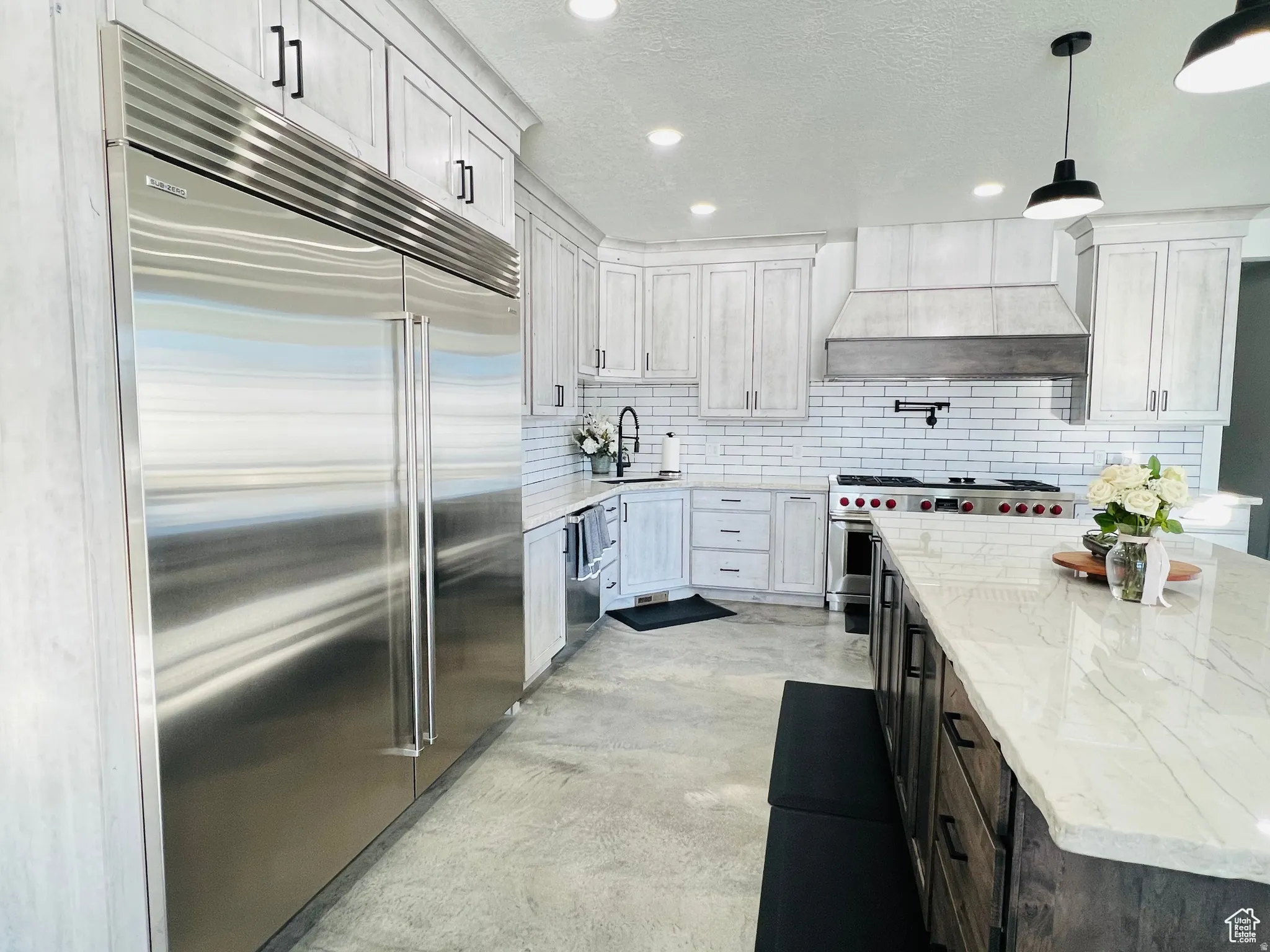 Kitchen with premium appliances, concrete flooring, light stone counters, a textured ceiling, and hanging light fixtures