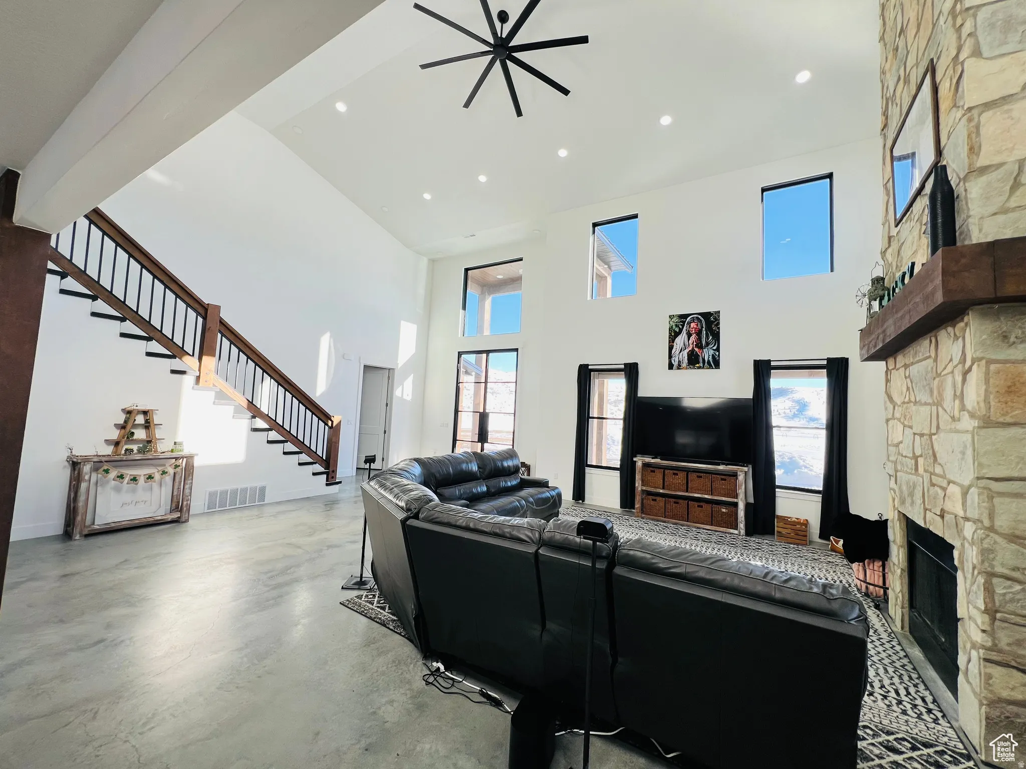 Living area with a high ceiling, a stone fireplace, finished concrete flooring, recessed lighting, and a ceiling fan