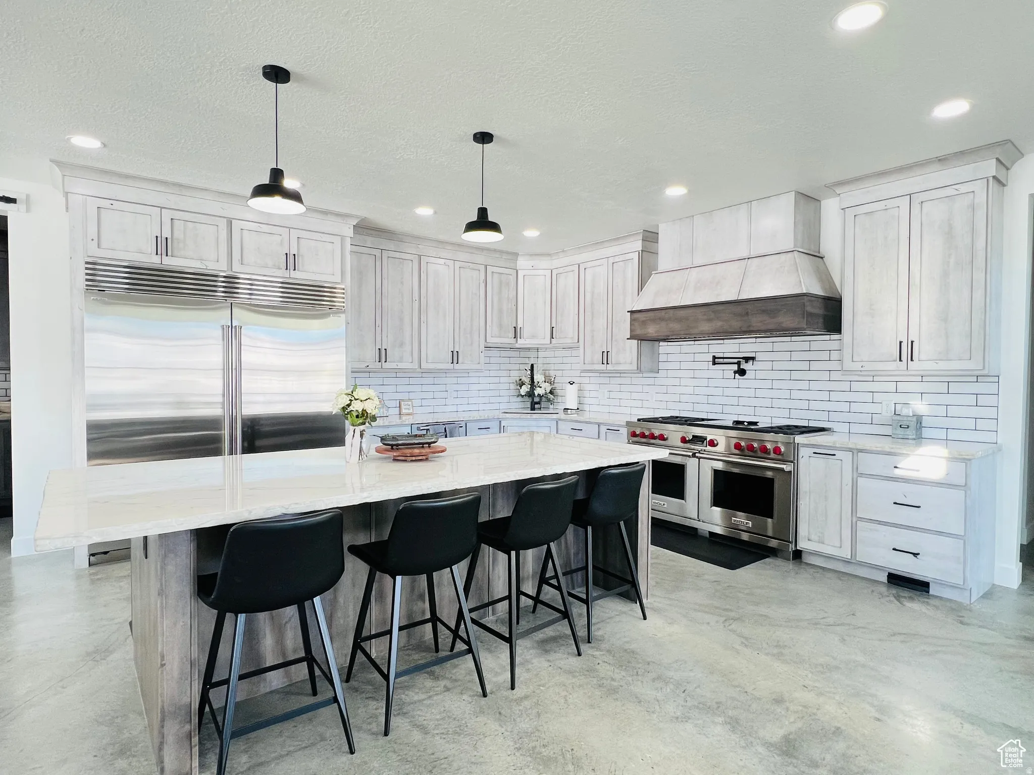Kitchen with premium appliances, light stone counters, a kitchen breakfast bar, concrete flooring, and hanging light fixtures