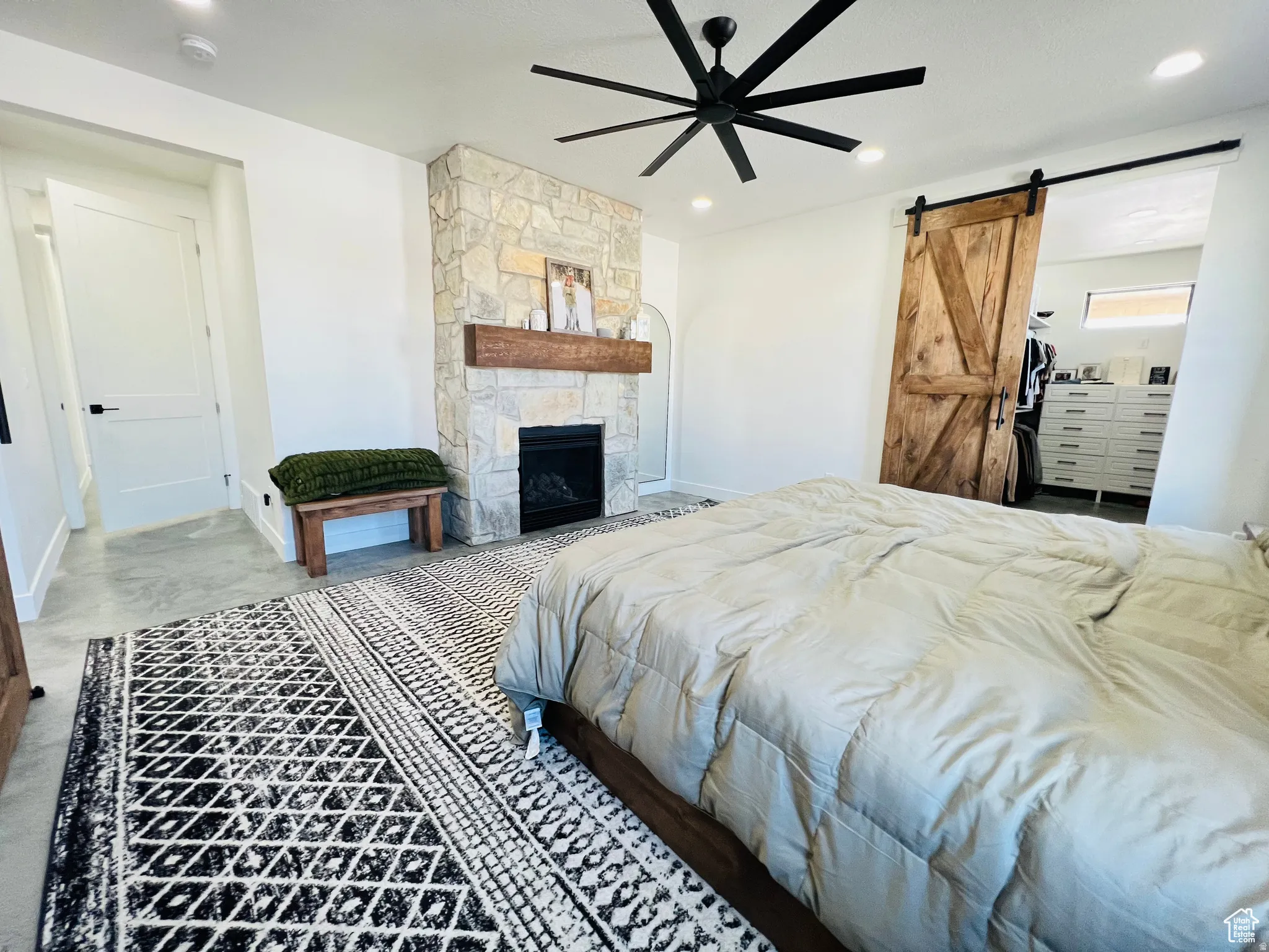 Bedroom with a barn door, a stone fireplace, a ceiling fan, and recessed lighting