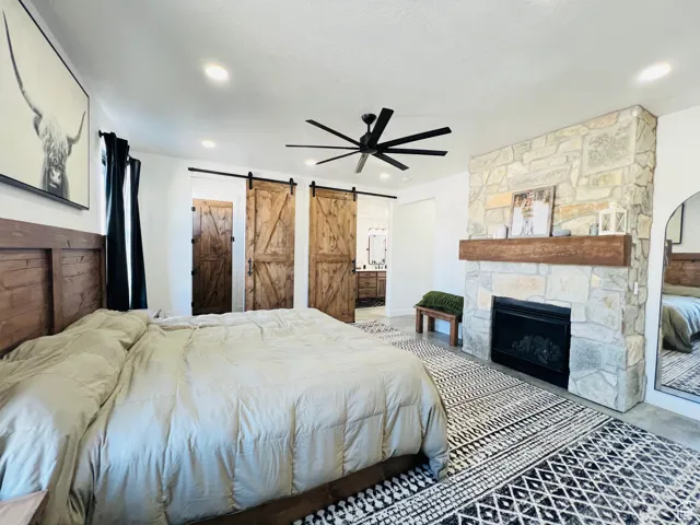 Bedroom with a barn door, a ceiling fan, a fireplace, and ensuite bath