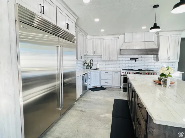 Kitchen with premium appliances, concrete flooring, light stone counters, a textured ceiling, and hanging light fixtures