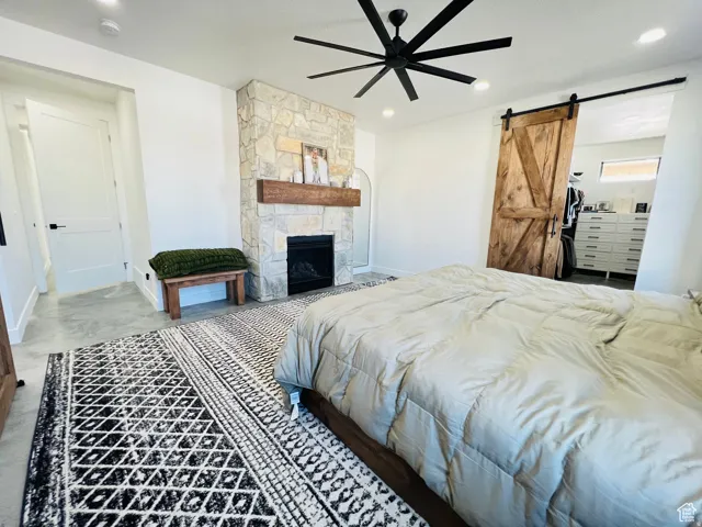 Bedroom with a barn door, a stone fireplace, a ceiling fan, and recessed lighting