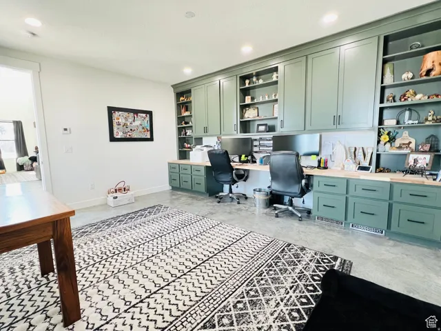 Home office with built in study area, built in features, recessed lighting, and concrete floors