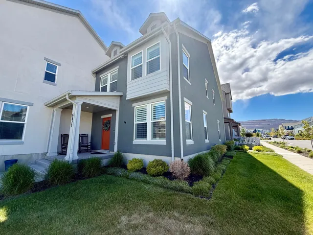 Two-story stucco and siding residence featuring a covered entryway with columns, an orange front door with a wreath, multiple windows with white frames and plantation shutters, and a manicured lawn with established landscaping