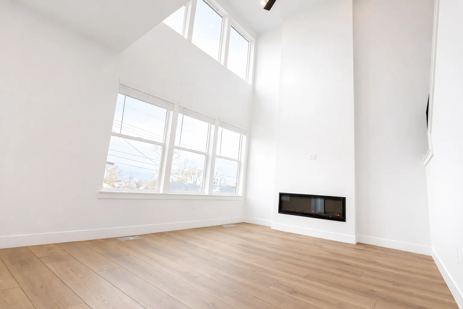 Unfurnished living room featuring a high ceiling, light wood-style floors, and a glass covered fireplace