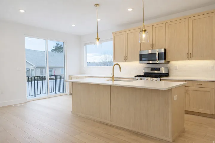 Kitchen with light wood finish cabinetry, stainless steel appliances, backsplash, a center island with sink, and pendant lighting