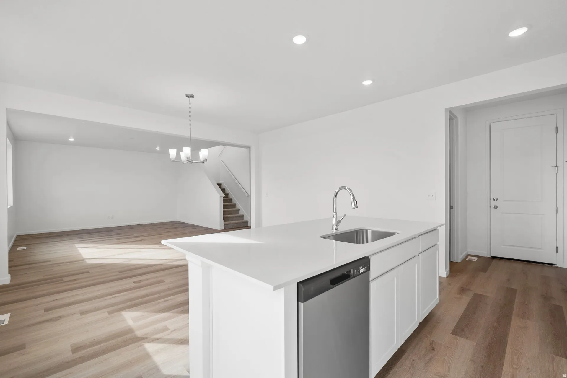 Kitchen featuring stainless steel dishwasher, white cabinetry, a center island with sink, and light wood-style flooring