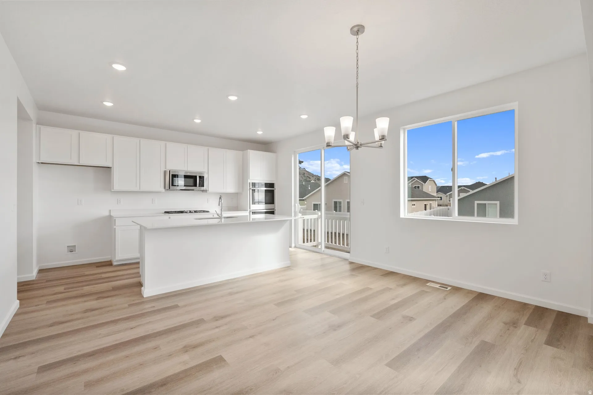 Kitchen featuring white cabinets, suspended lighting, light wood finished floors, a center island with sink, and stainless steel microwave