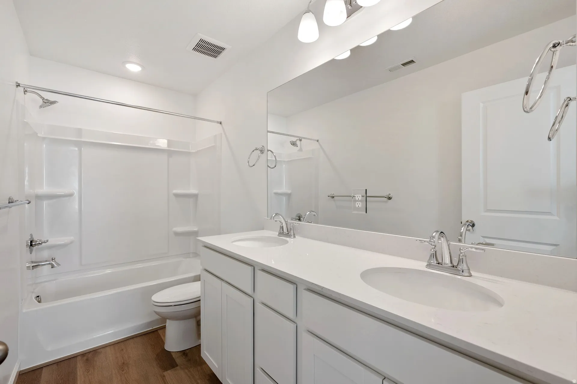 Bathroom featuring double vanity, dark wood finished floors, and bathing tub / shower combination